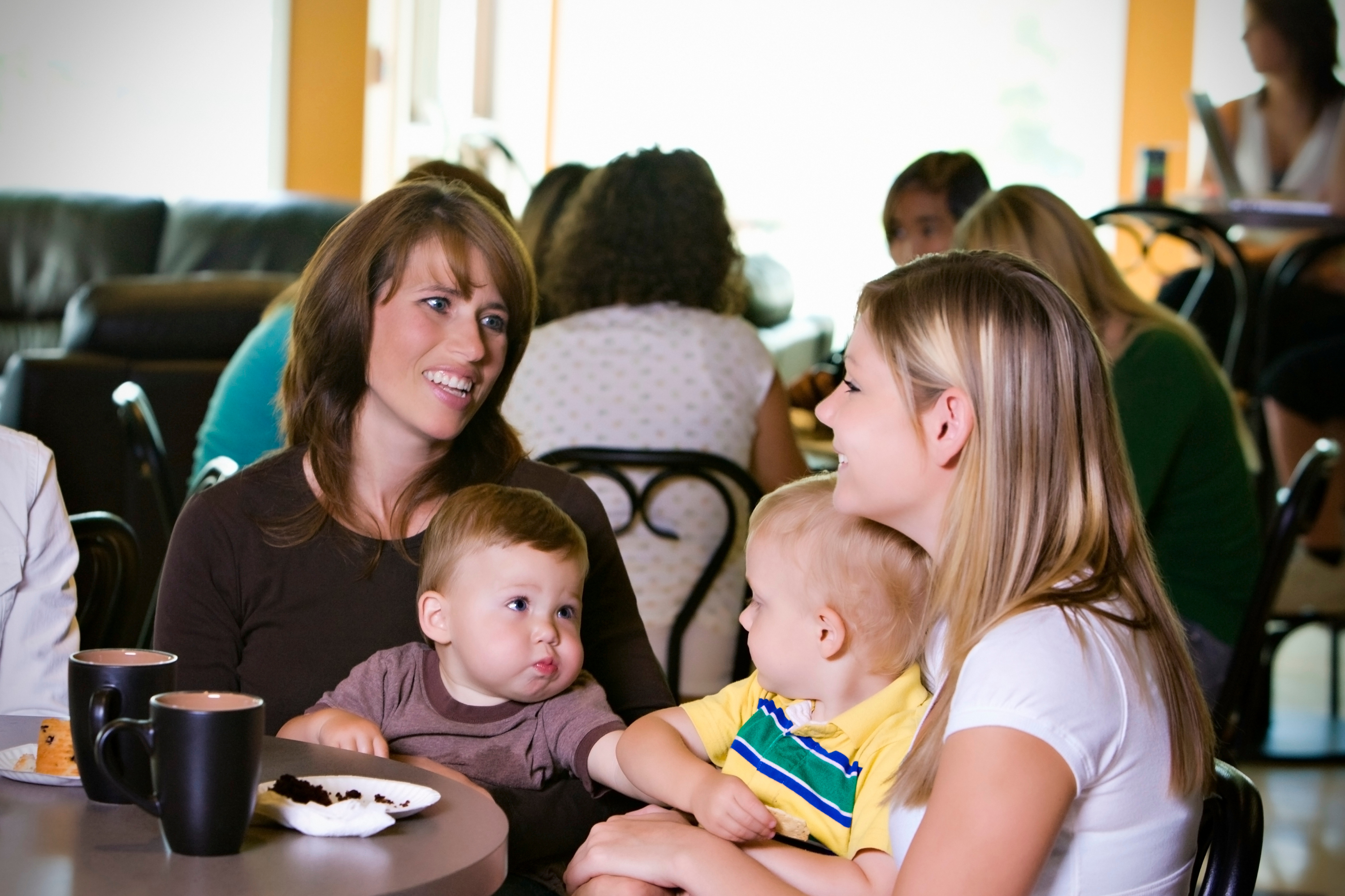 Two mums with their babies, sat a table and talking.