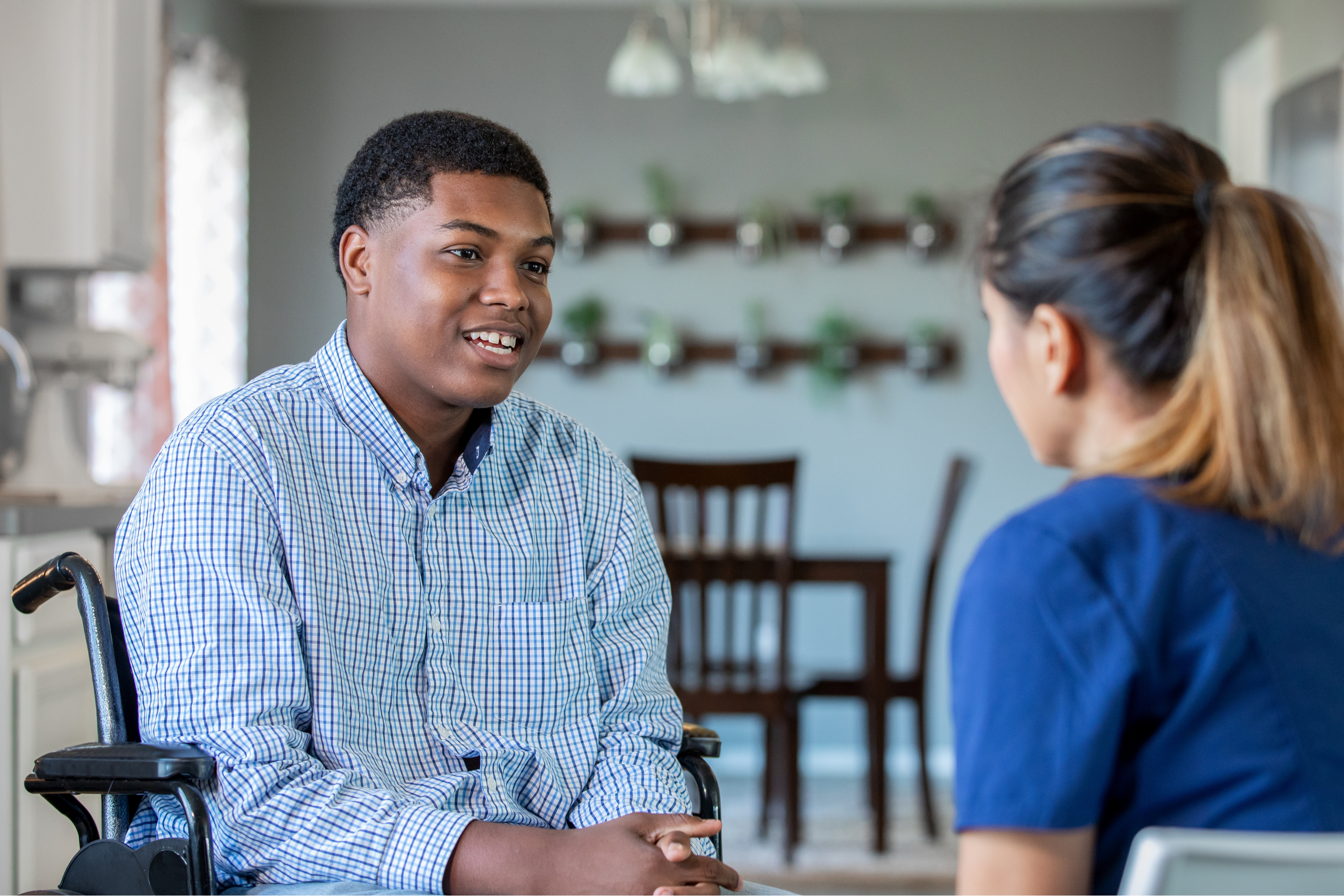 A young man in a wheelchair talking to a healthcare worker.