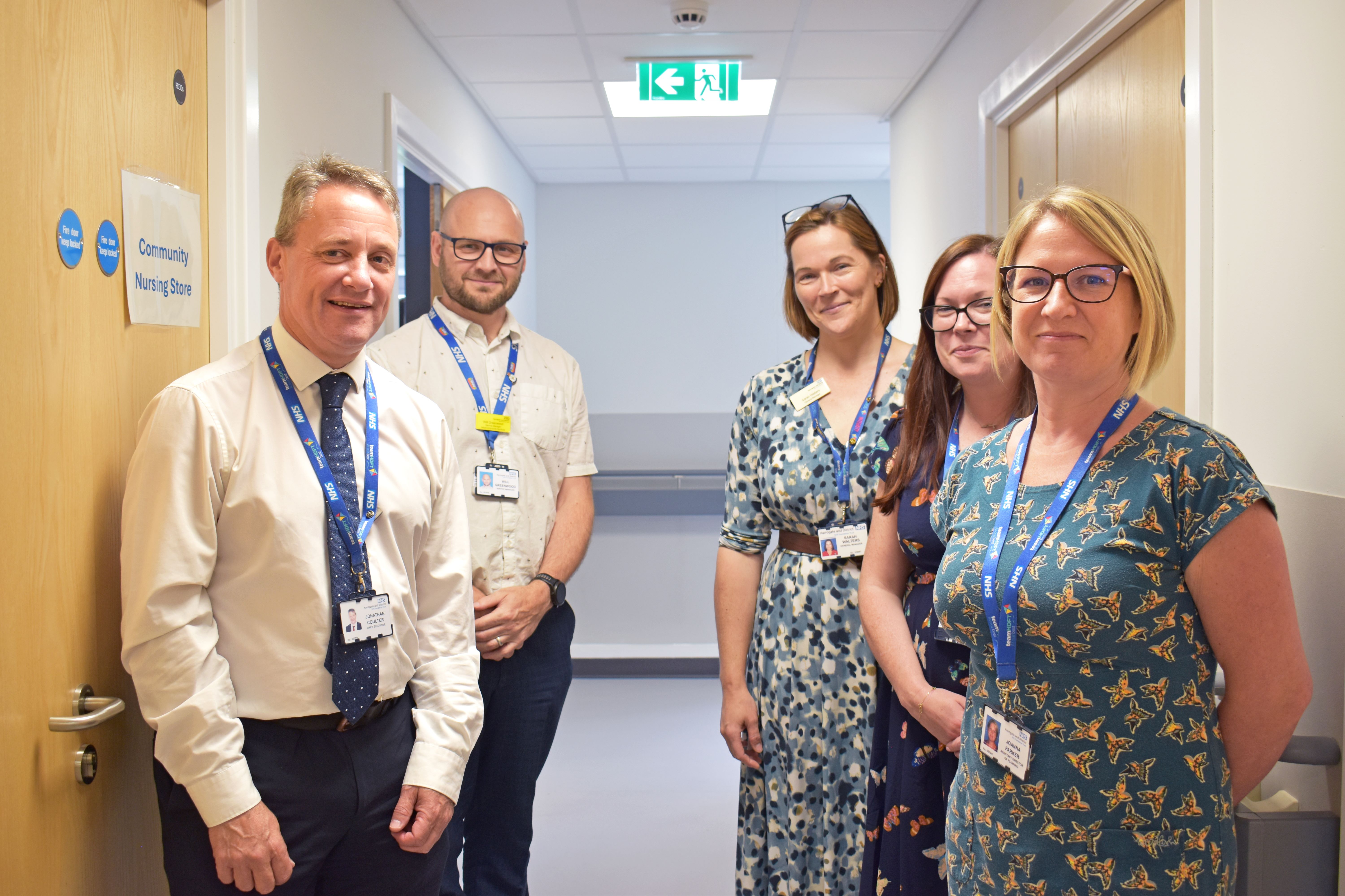 Five healthcare staff smiling in a hospital corridor.