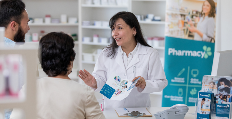 A pharmacist showing two customers a leaflet and explaining their services to them.