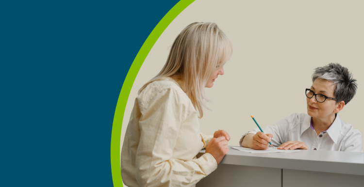 A receptionist at a GP practice' reception desk talking with a patient.