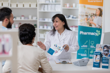 A pharmacist showing two customers a leaflet and explaining their services to them.