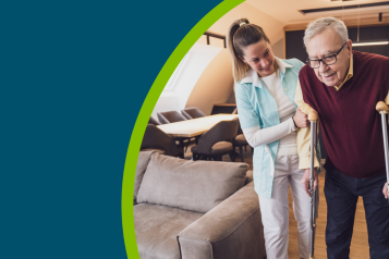 Home caregiver supporting an older man on crutches in his home.