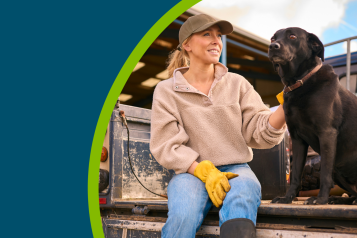 Female farm worker sitting on tailgate of off road farm vehicle with dog
