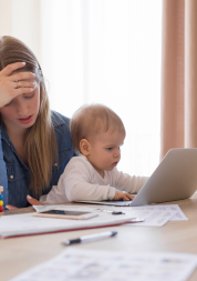 A mother looking stressed with her head in her hand whilst holding her baby with the other.